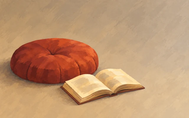 An open book rests close to a single cushion surrounded by broad empty space.